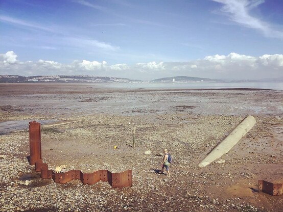 Looking across Swansea bay from Mumbles, low tide - mud, silt, stone bedrock, sea, industry, pipes, piers, rusted remnants, and pipes. As people still flock in sun to walk it’s open shores and open blue skies.