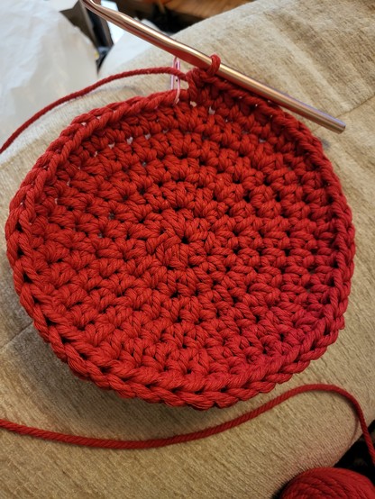 Base of a macrame crochet basket, bright red, with the gold hook visible at the back. 