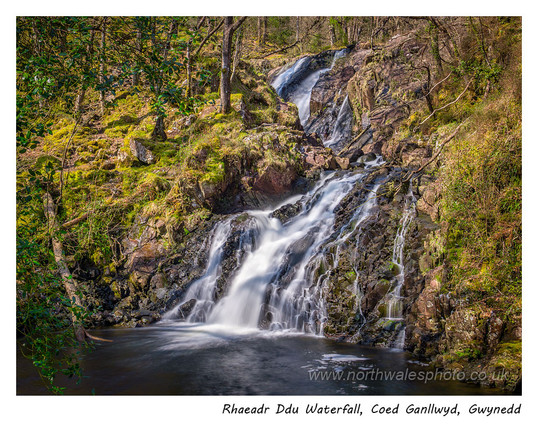 A waterfall in woodland with another higher fall visible in the background.