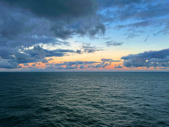 Late evening  pews over a calm sea with dark clouds starting the build and the last of the sunset showing as a bright yellow and orange sky over the horizon. 