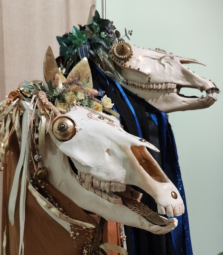 Two Mari Lwyd figures - a Welsh tradition involving singing, drinking and people disguised with sheets and horse skulls. These two have piles of ribbons and leaves on their heads, and baubles for eyes. 