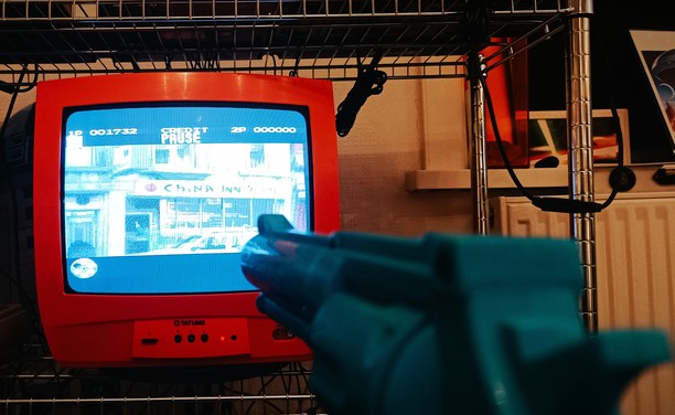 "Lethal Enforcers" videogame playing on a 14" CRT screen. The TV is bright orange and the sky blue "Justifier" lightgun protrudes into shot.