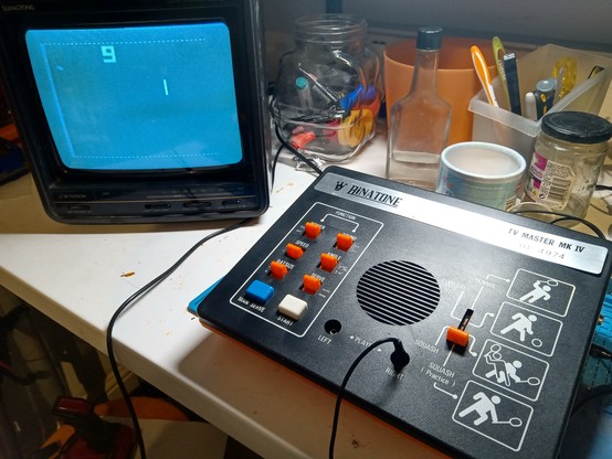 1970s Binatone "Pong" console on a cluttered workbench. The "Squash Practice" mode can be seen playing on a small monochrome CRT screen.
