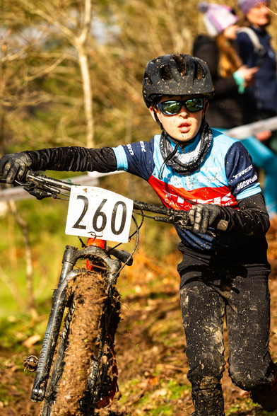 Boy walking with a very muddy mountain bike