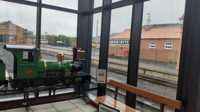 A view from inside a railway museum. To one side, inside is a narrow gauge loco, and outside is a sign reading Aberystwyth 