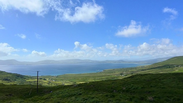 Looking down the slopes of one hill to a bay, with more hills on the far side. Again, there's lots of blue sky and fluffy clouds, all the green you could imagine, and glorious blue water.