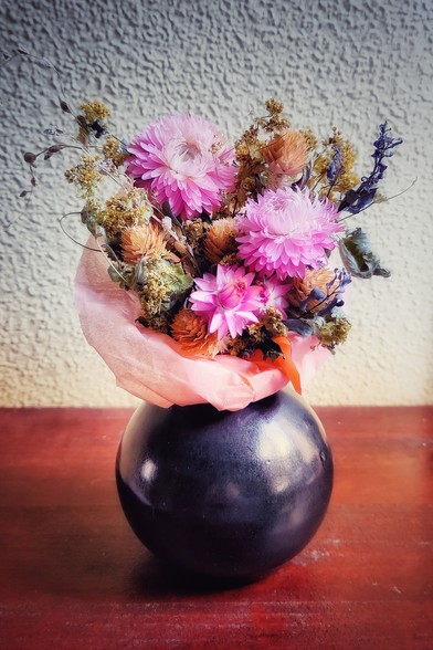 A small bunch of eternal flowers in a round vase.