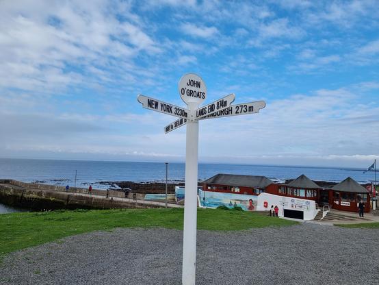The signpost at John o' Groats North Scotland, showing the white sign, a bit of the harbour, blue sky with clouds