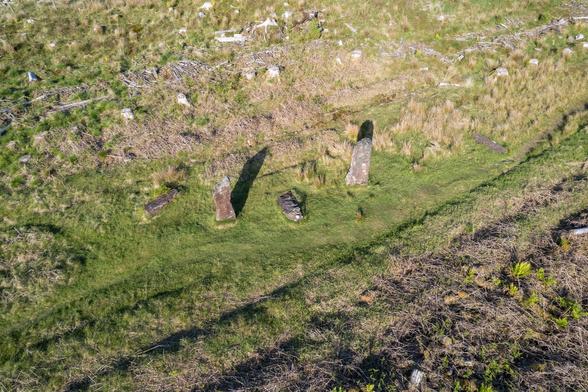 Drone photograph of the Kilmore Standing Stones near the village of Dervaig on the Isle of Mull, showing 2 upright stones and 3 lying down in scrubby ex foresty land, grey skies
