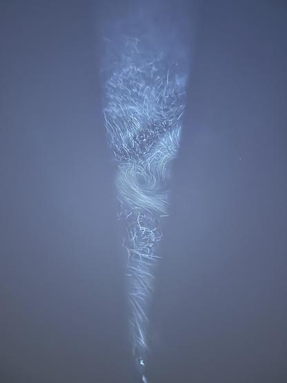 Swirling patterns of fog particles caught in the cone of light from a flashlight, it’s a mix of in focus particles and smoke-like swirls