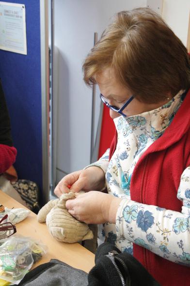 Ann, a woman with light skin tone and short brown hair, looking down at a small teddy which she is sewing up.