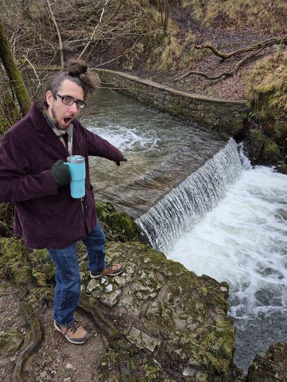 Chris standing, looking shocked, and pointing to a modest waterfall.