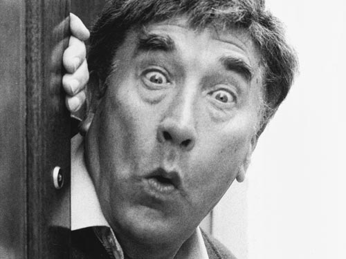 A black and white image of Frankie Howerd pulling an "ooh err missus" face