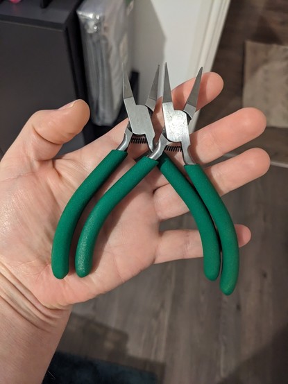 A pair of duck bill pliers with green handles.