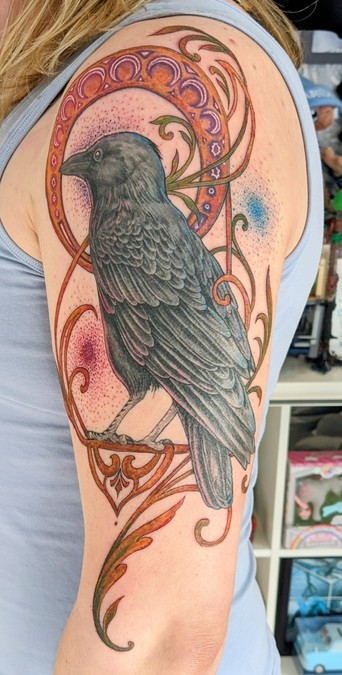 An art nouveau style tattoo on my upper arm featuring a crow, and glowing pinks and blues