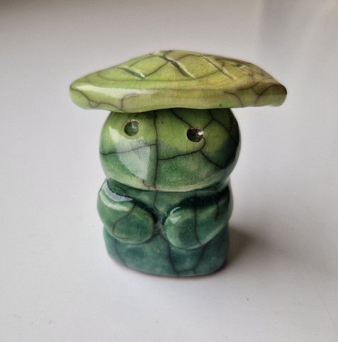 A little nature spirit statue with a leaf on its head. A soft, rounded form with a gentle, peaceful expression. Fired with a crackle glaze in shades of green.