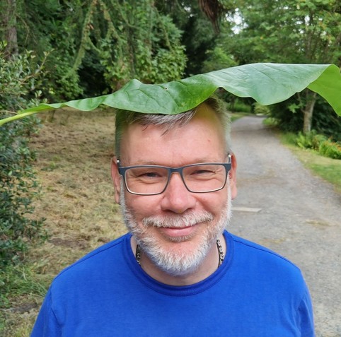 Mike in a blue t-shirt on a path through the trees. He's got a massive magnolia leaf on his head. 🍃😊