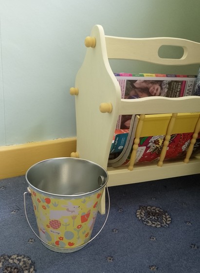 A small metal bucket is placed on a blue carpet just to the side of a wooden magazine rack which has been repainted in two-tone yellows. The outside of the bucket is printed with a Easter-themed montage of white cravat-wearing rabbits, painted eggs and flowers. It's underlying colour is a similar shade of yellow to the darker one on the magazine rack, but it does still look a little muted compared to the vivid yellow of my skirting boards. I like yellow!