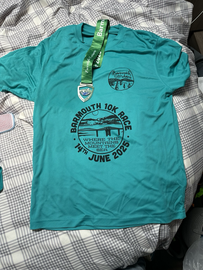 A picture of a t-shirt for the Barmouth 10k race, 2025. Maybe it’s blue. Maybe it’s green. Maybe it’s turquoise. 