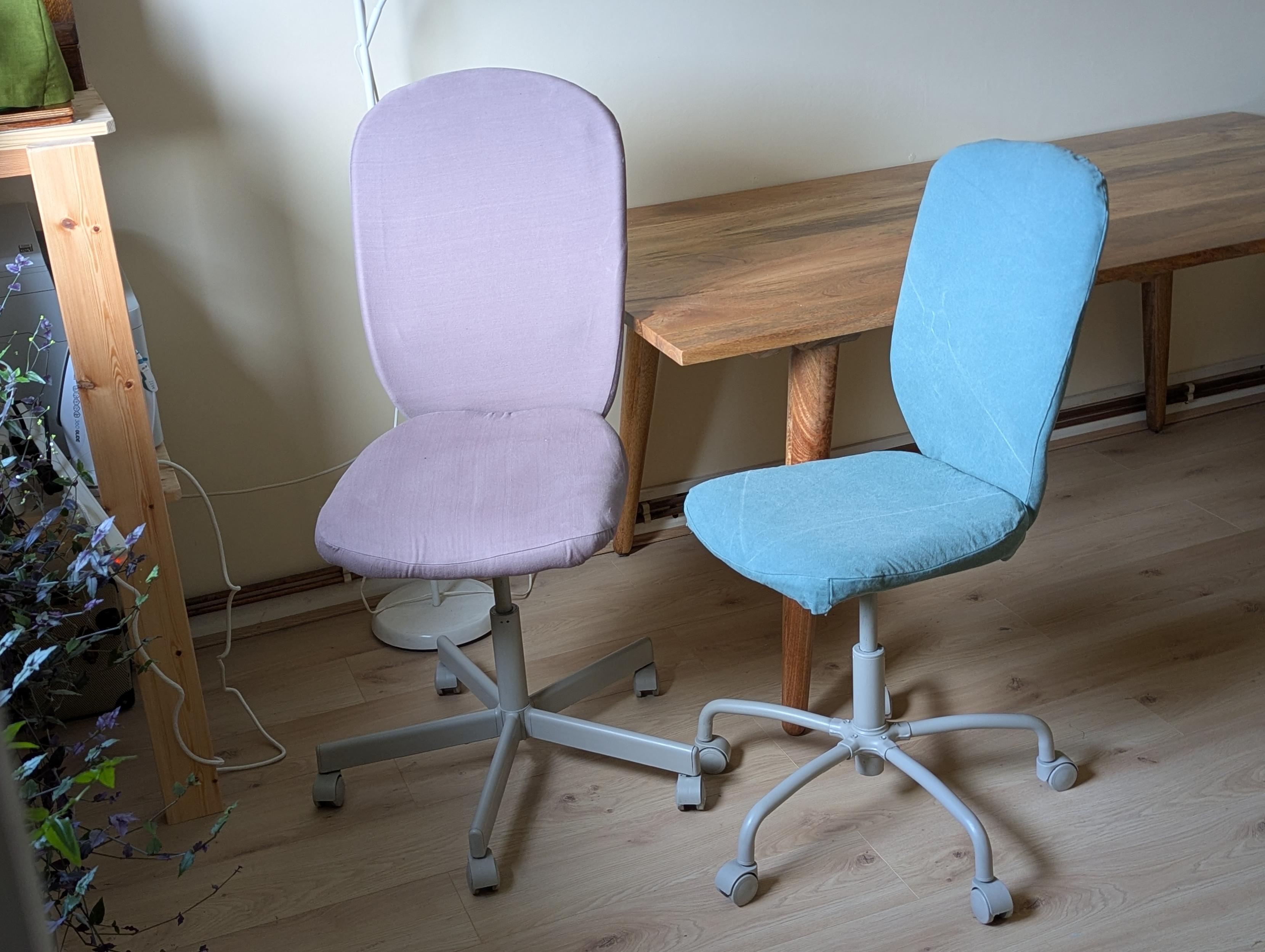 Two desk chairs. One has a soft purple cover, the other light blue. Both have light grey legs and wheels.