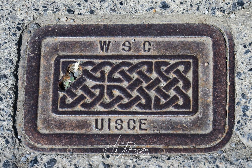 On the pavement in Doolin, there are traditional access points for services. This is a beautifully detailed water access point, with a Celtic design in the centre of the heavy metal. The word UISCE [water[ on the lower part, and W S C on the upper.
